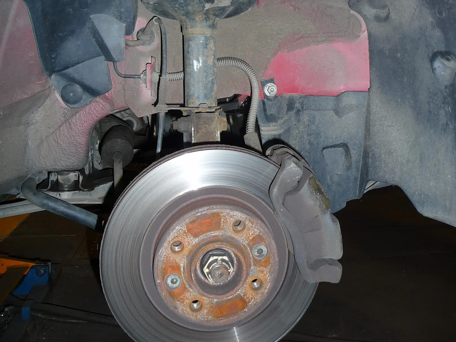 Train avant d'une Renault avec jambe de force, ressort et disque de frein visibles en atelier