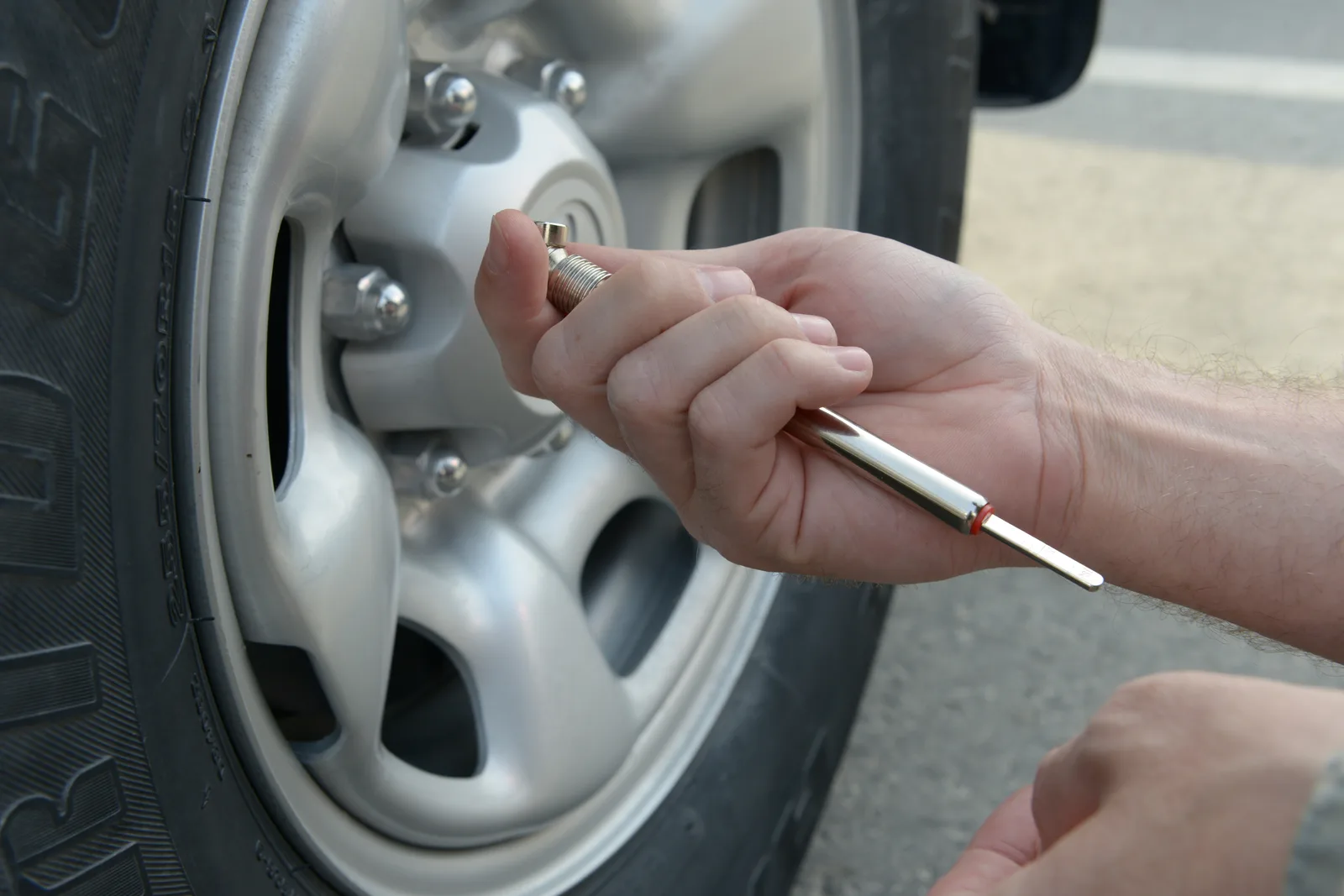 Conducteur vérifiant la pression d'un pneu avec un manomètre crayon appliqué sur la valve